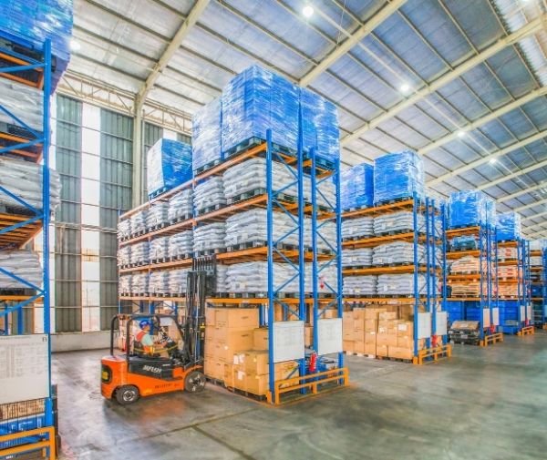 Forklift transporting palletized inventory in a large warehouse with high-density storage racks