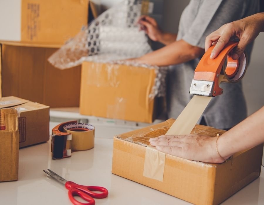 Worker packing cardboard boxes with tape and bubble wrap, adding value through secure and efficient packaging for safe product handling and delivery